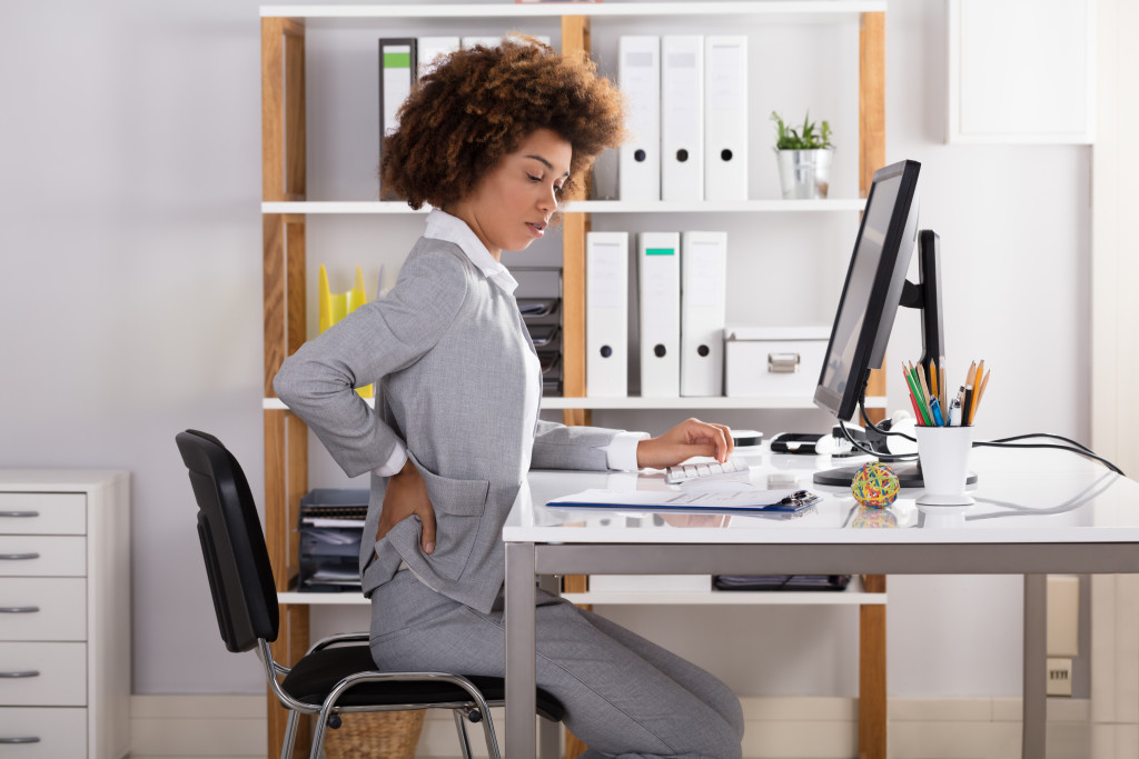 an office lady holding her lower back while sitting in an office desk