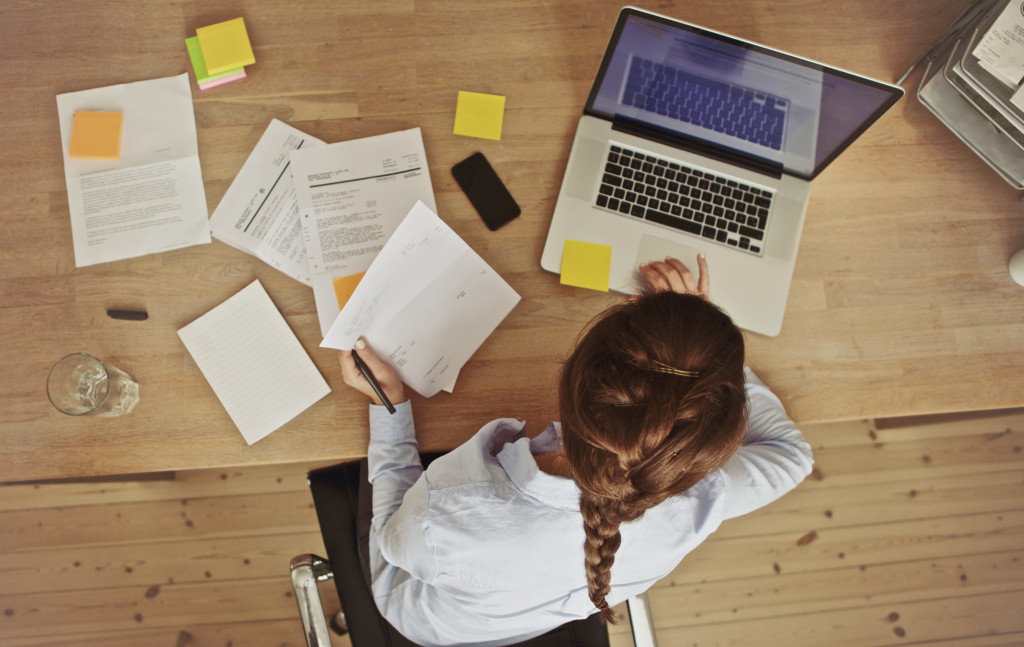 a woman with sticky notes and documents all over her desk while working on laptop
