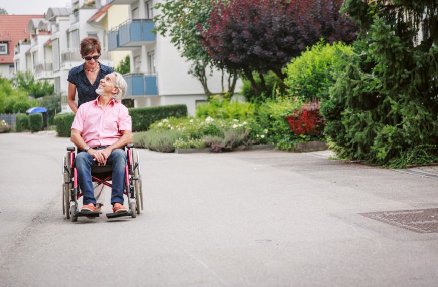 Senior adult on a wheelchair pushed by a female caregiver.