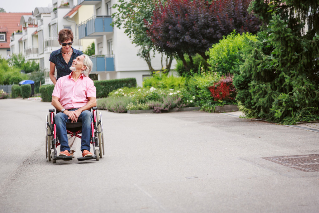 Senior adult on a wheelchair pushed by a female caregiver.