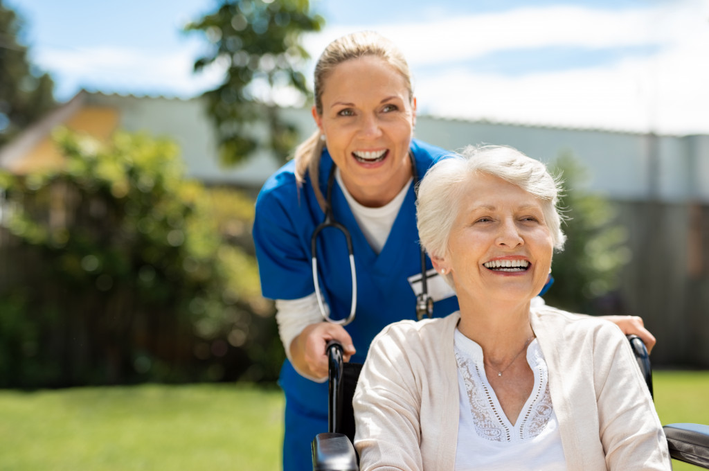 Happy senior female on a wheelchair with a nurse behind her.