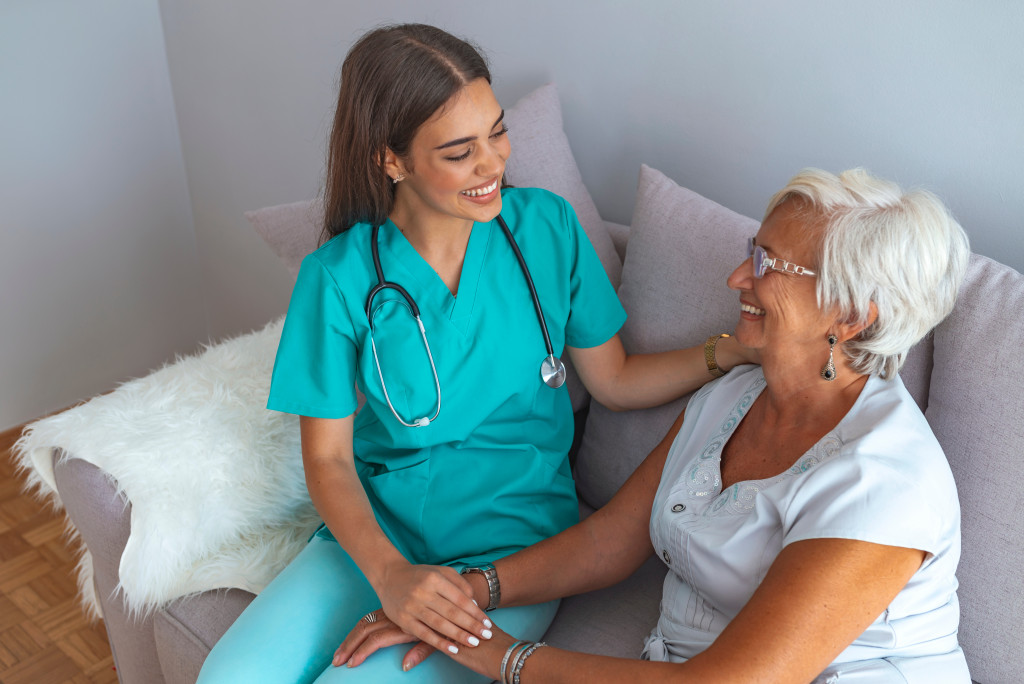 Senior female smiling at a female caregiver inside a home.