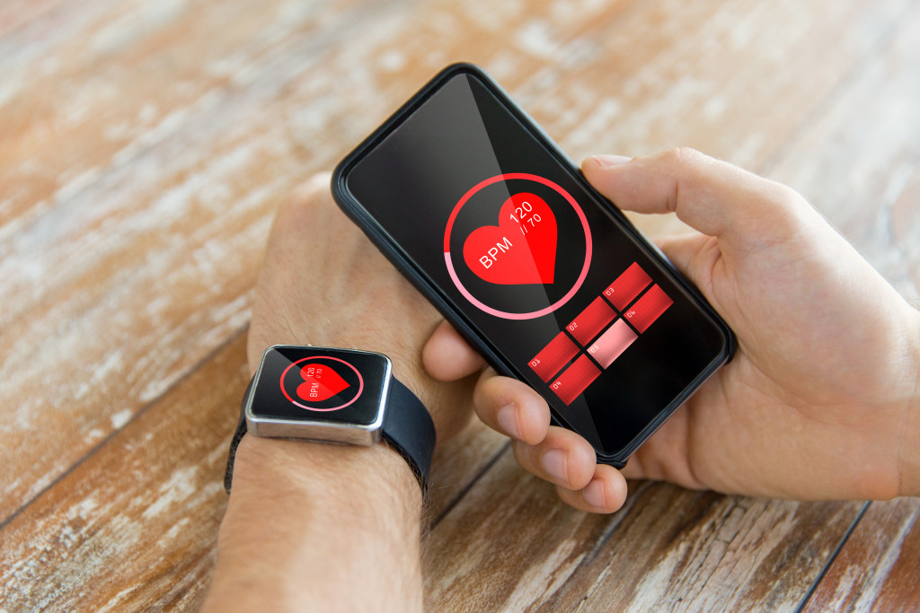 Young man holding a smartphone while wearing a smart watch that shows a red heart icon.